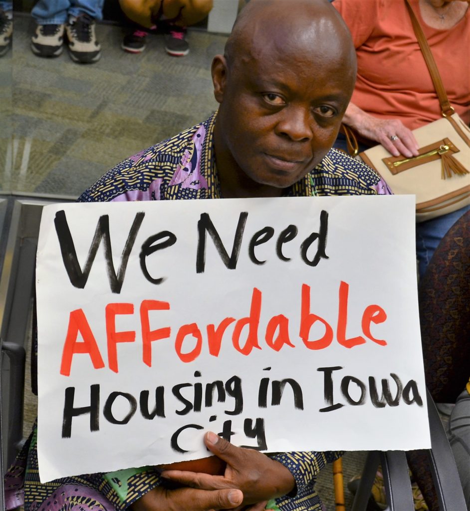 A man holding up a sign that says " we need affordable housing in iowa city ".