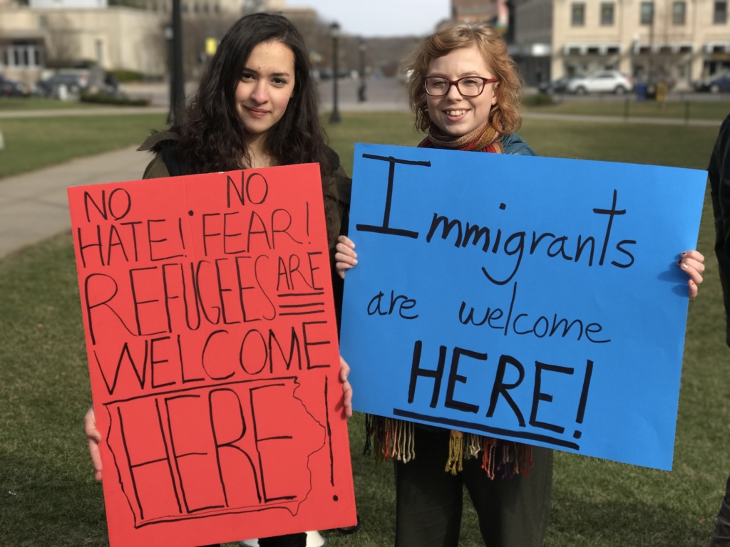 Two women holding signs that say " immigrants welcome here ".