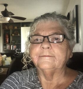 A woman with glasses is sitting in front of a wall.