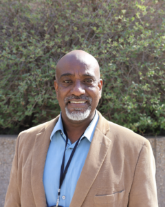 A man in a brown jacket and blue shirt.